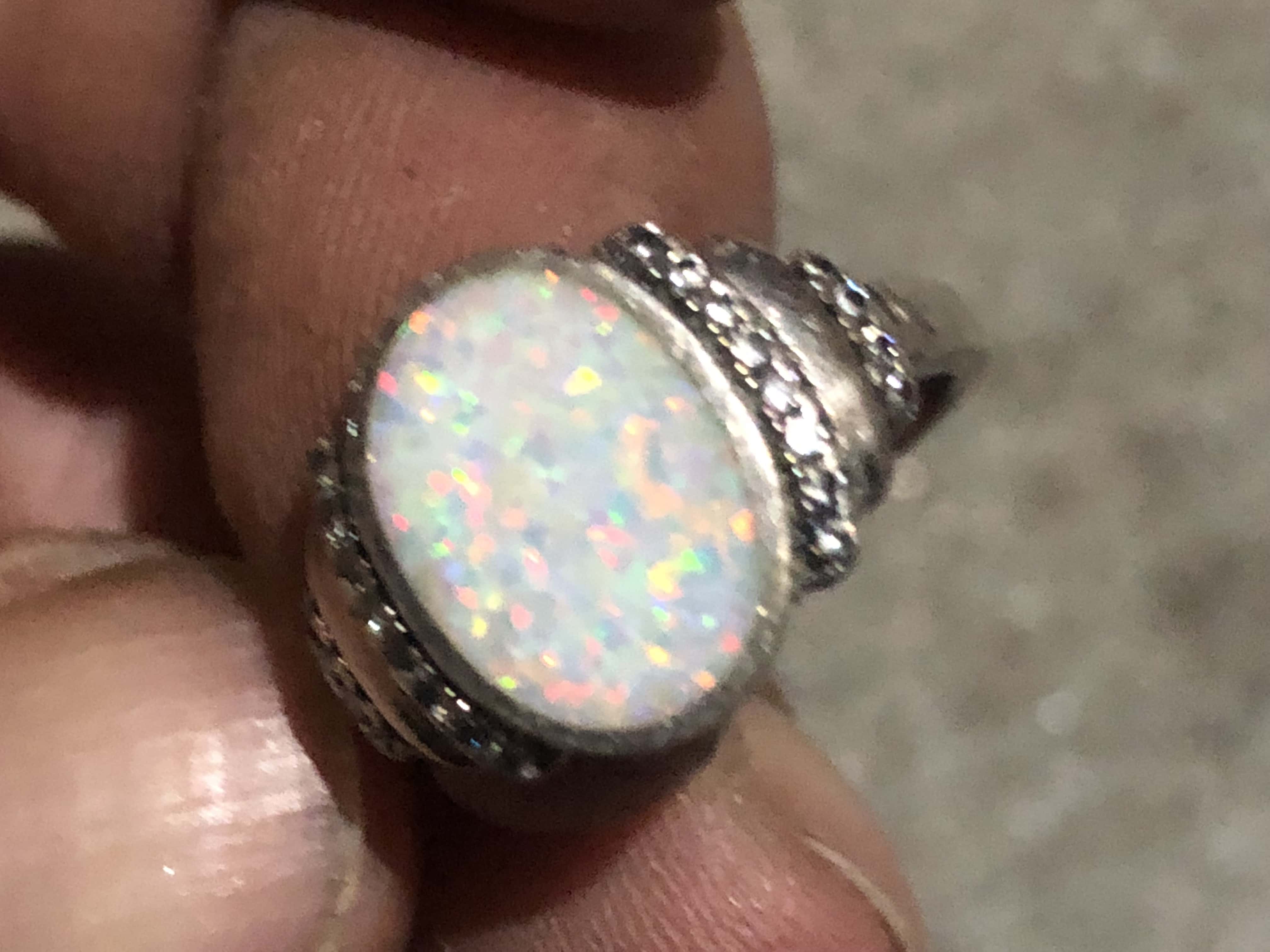 Opal Looking Gem Ring with Silver Metal Band Inset with Diamonds Held Up Close in Fingers