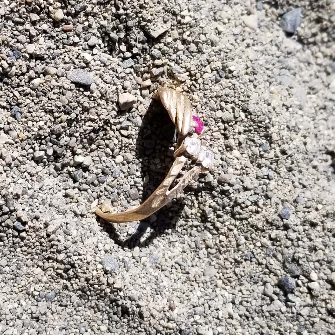 Ring in Loose Gravel Sand Find Spot with Three Dusty gems and Hand Shape Visible