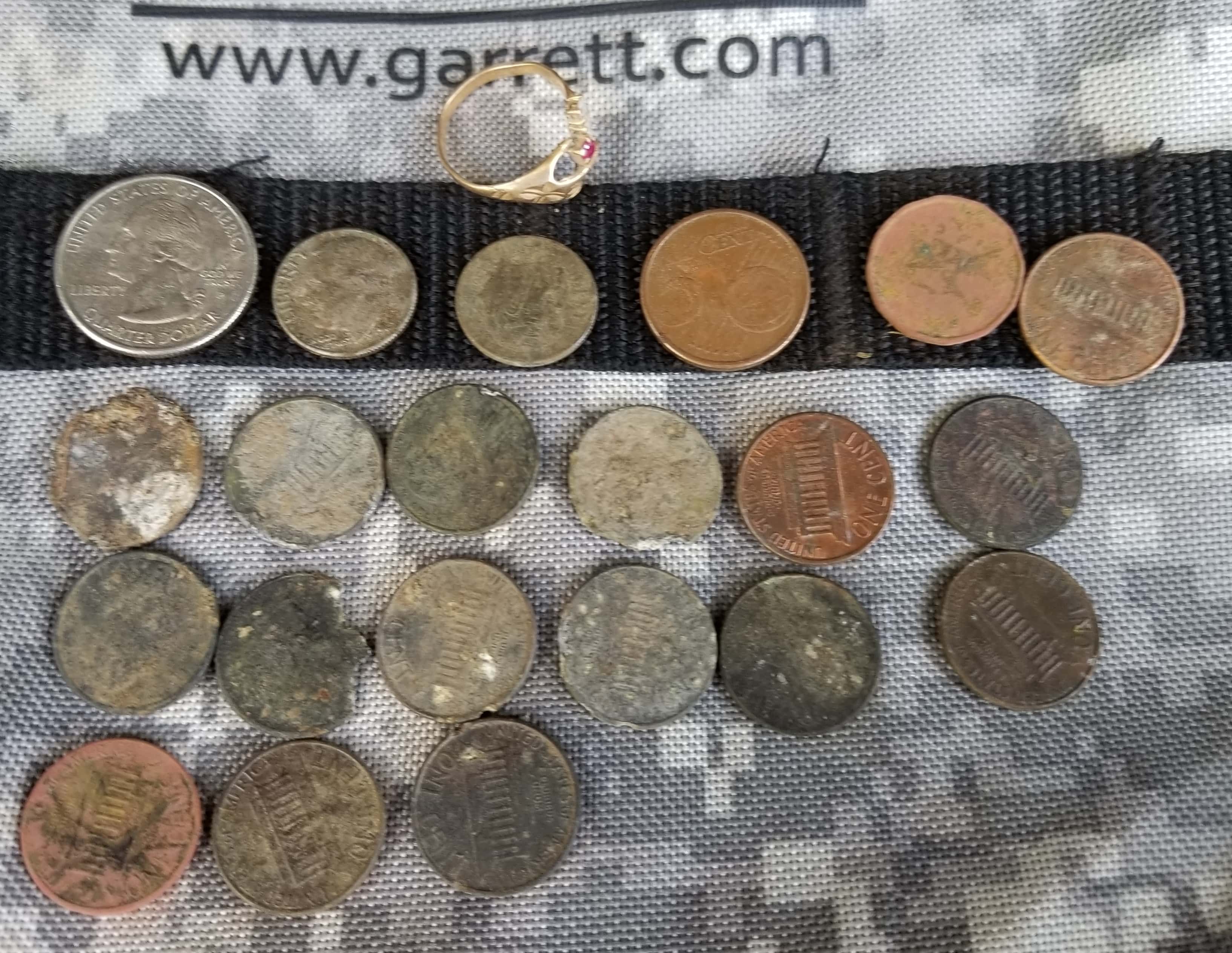 Pennies and Coins Lined Up in a Grid with Ring at the Upper Left Corner on Garrett Camo Bag Fabric Background