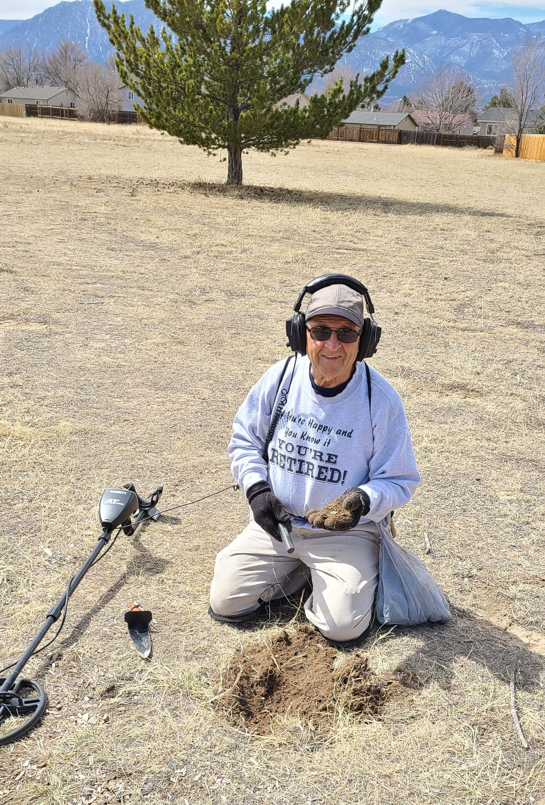 Man Holding Finds with Metal Detector and Pinpointer on Straw Strewn on Ground and Digger beside Metal Detector