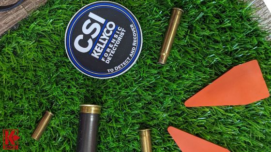 Image of CSI Evidence Marking equipment around bullet casings and Kellyco CSI sticker on faux grass.